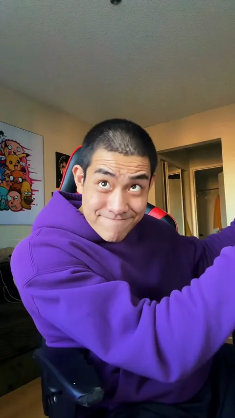 AI-generated ABCDEFG I Need Money video frame: a young man with a buzz cut in a purple hoodie in a gaming chair rolls his eyes up and smirks